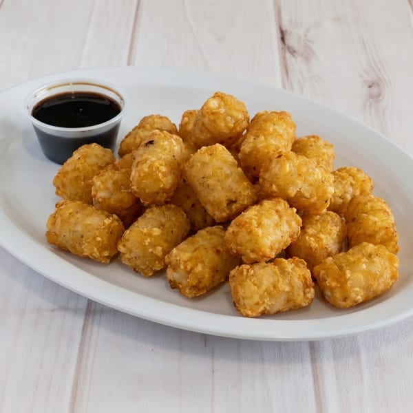 A white oval plate filled with golden-brown tater tots and a small cup of dark dipping sauce.