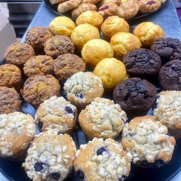 A black tray filled with assorted muffins, including blueberry, chocolate chip, and streusel-topped varieties.