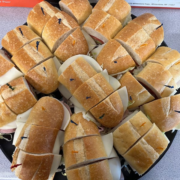 A platter of sliced submarine sandwiches with various fillings, garnished with colorful toothpicks.