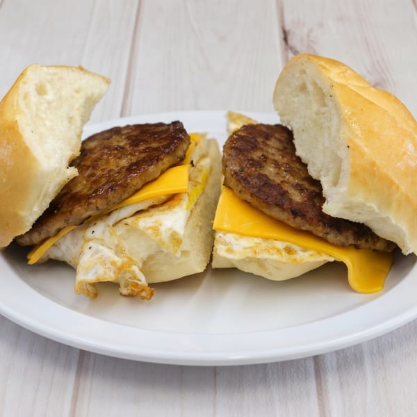 Two halves of a breakfast sandwich with sausage, egg, and cheese on a white plate.