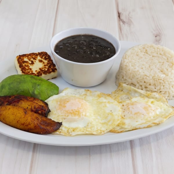 A white plate with fried eggs, rice, black beans, avocado, fried plantains, and grilled cheese.